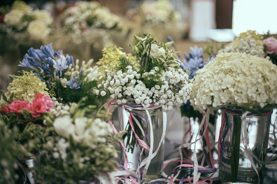A collection of fresh floral arrangements displayed in clear glass vases, featuring predominantly white hydrangeas and delicate white baby's breath, complemented by sprigs of pale yellow and soft pink